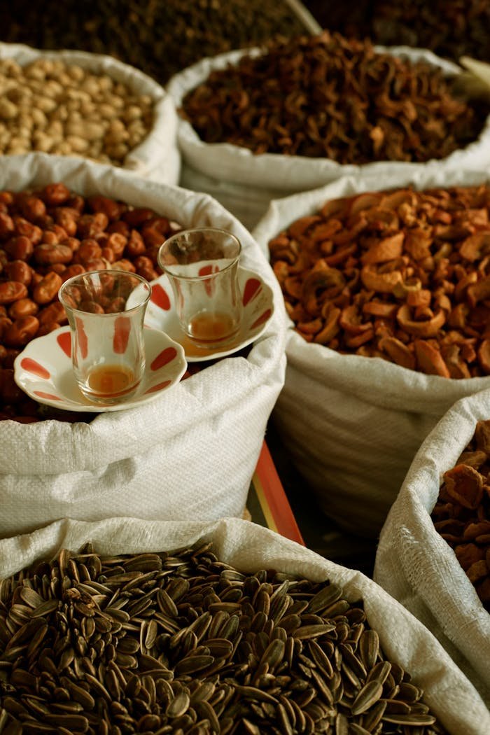 Vibrant selection of spices and seeds in sacks with two glass cups, creating a rich visual feast.